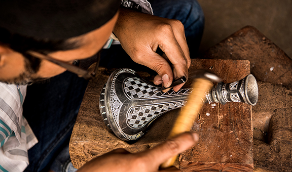 Bidar, Karnataka, India/ December 8, 2018: A Bidri craftsman engraves a traditional design on a vase, its grooves which will then be filled with fine silver wire.