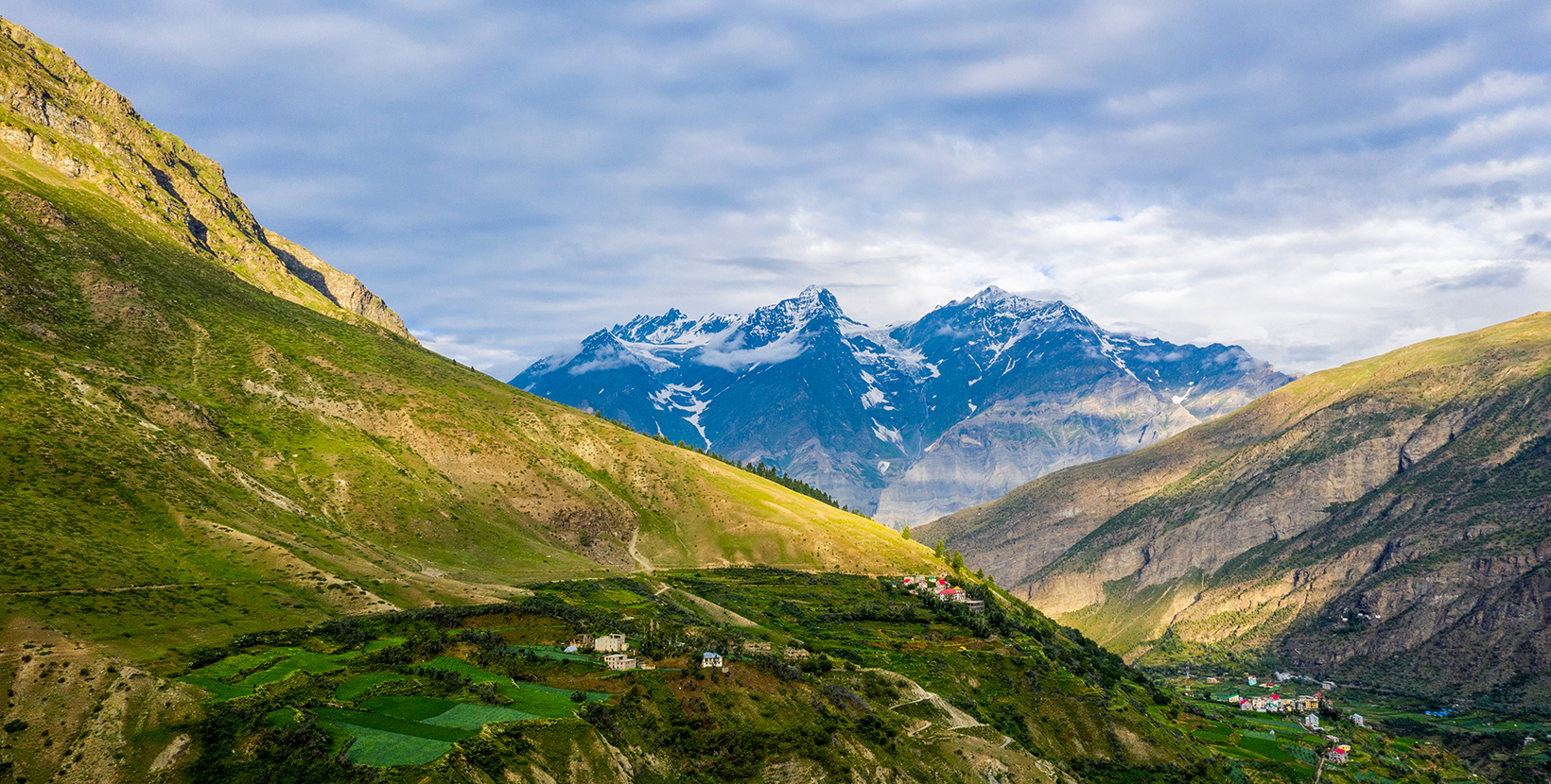 Beautiful mountains background. Mountainside village in the Himalayas valley at Keylong (Kyelang), Lahaul and Spiti district, India. Clouds over the snowy mountain peak.