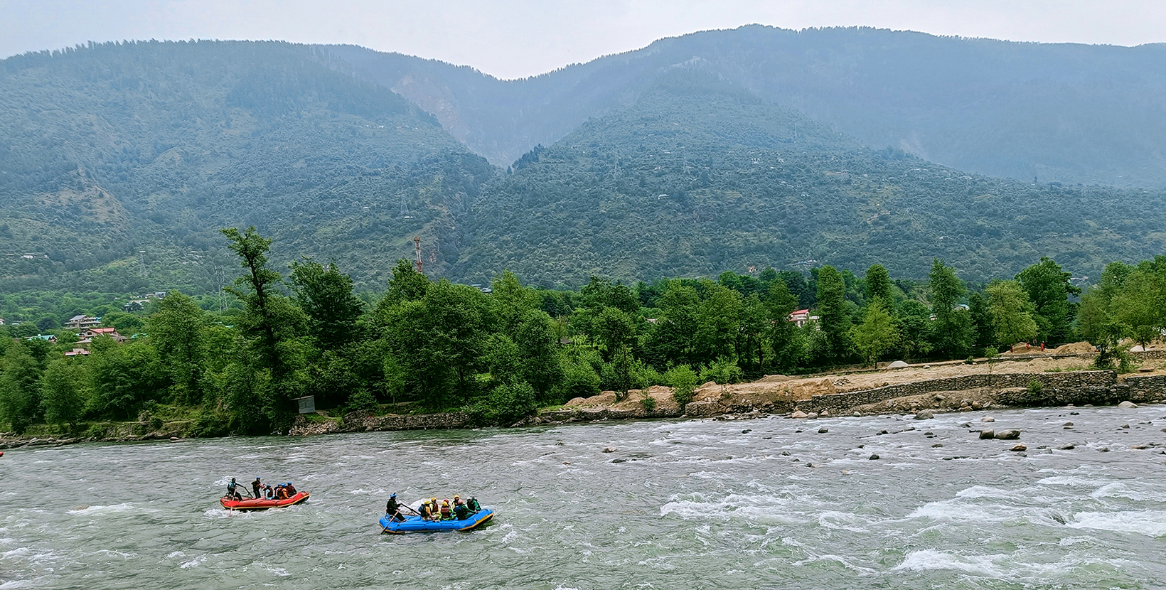 It can be seen in the picture that tourists are enjoying river rafting in the Beas River. The beautiful green mountains of Manali are visible in the background. 