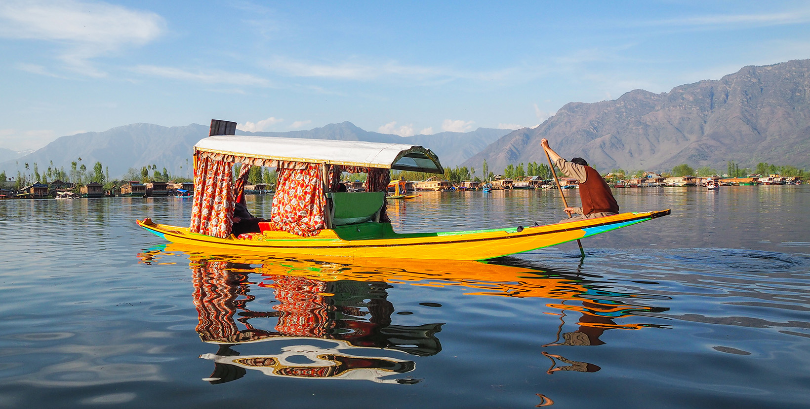 Beautiful view of Shikara boat ride on dal lake with houseboats and mountain background at Srinagar, Kashmir, India.