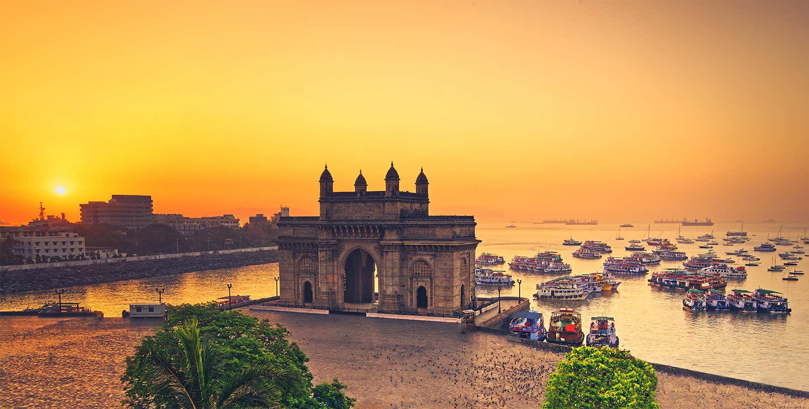 The gateway of India at sunrise with beautiful reflections in the sea. Boats in the water in a hot day.