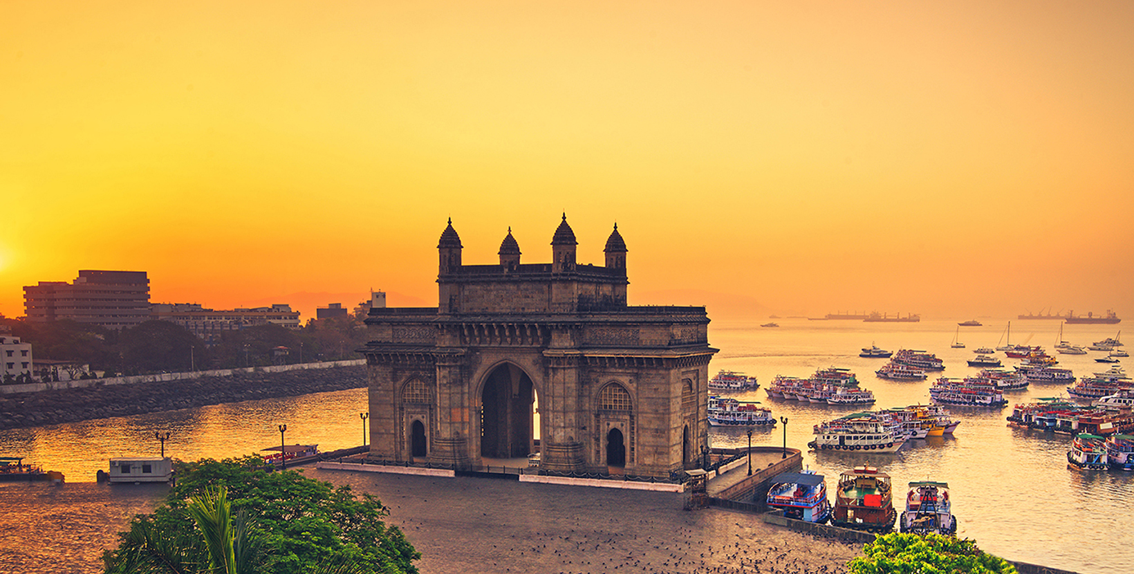 The gateway of India at sunrise with beautiful reflections in the sea. Boats in the water in a hot day.