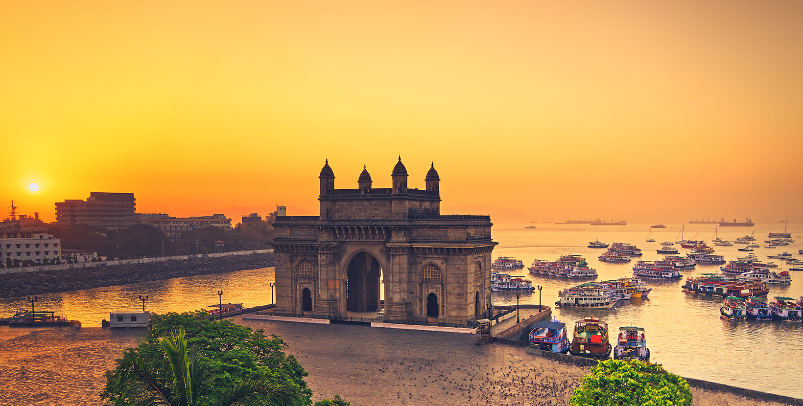 The gateway of India at sunrise with beautiful reflections in the sea. Boats in the water in a hot day.