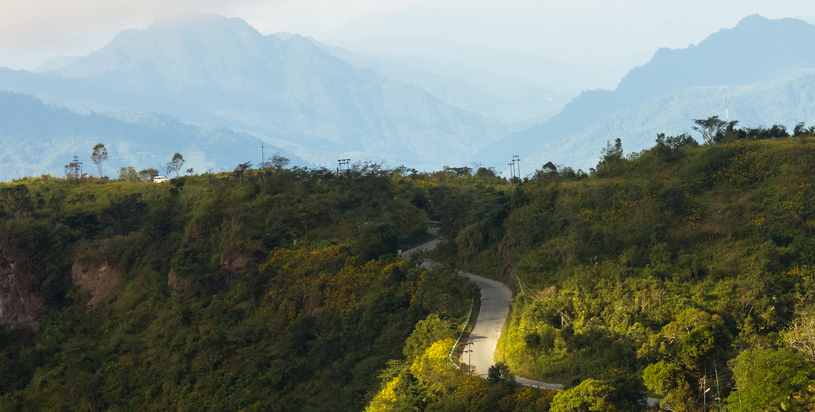 A road winds down the green hills that surround the city of Lunglei in Mizoram.