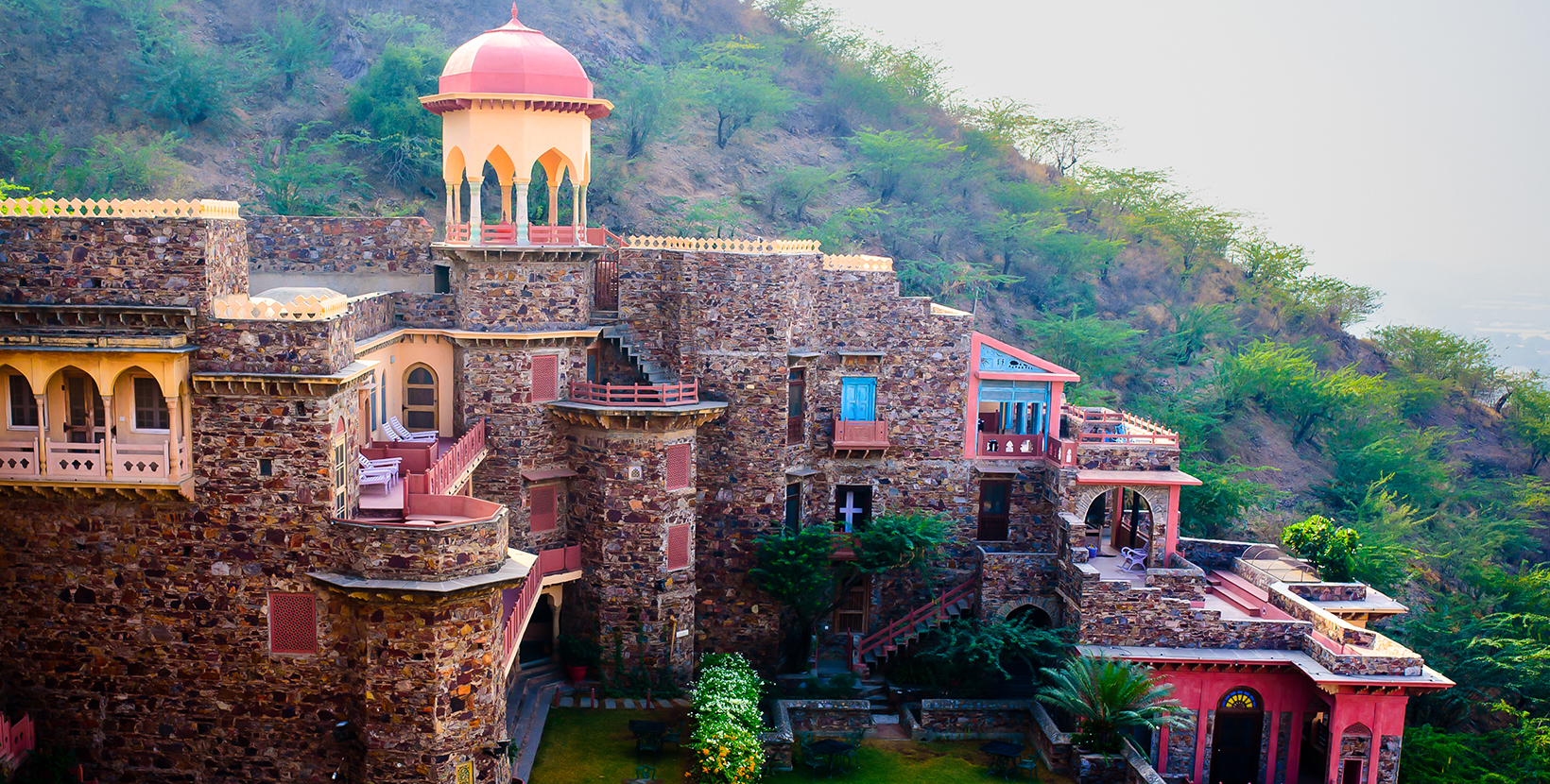 An old historical hill top fort on a mountain, with domes, arches and balcony with several windows.