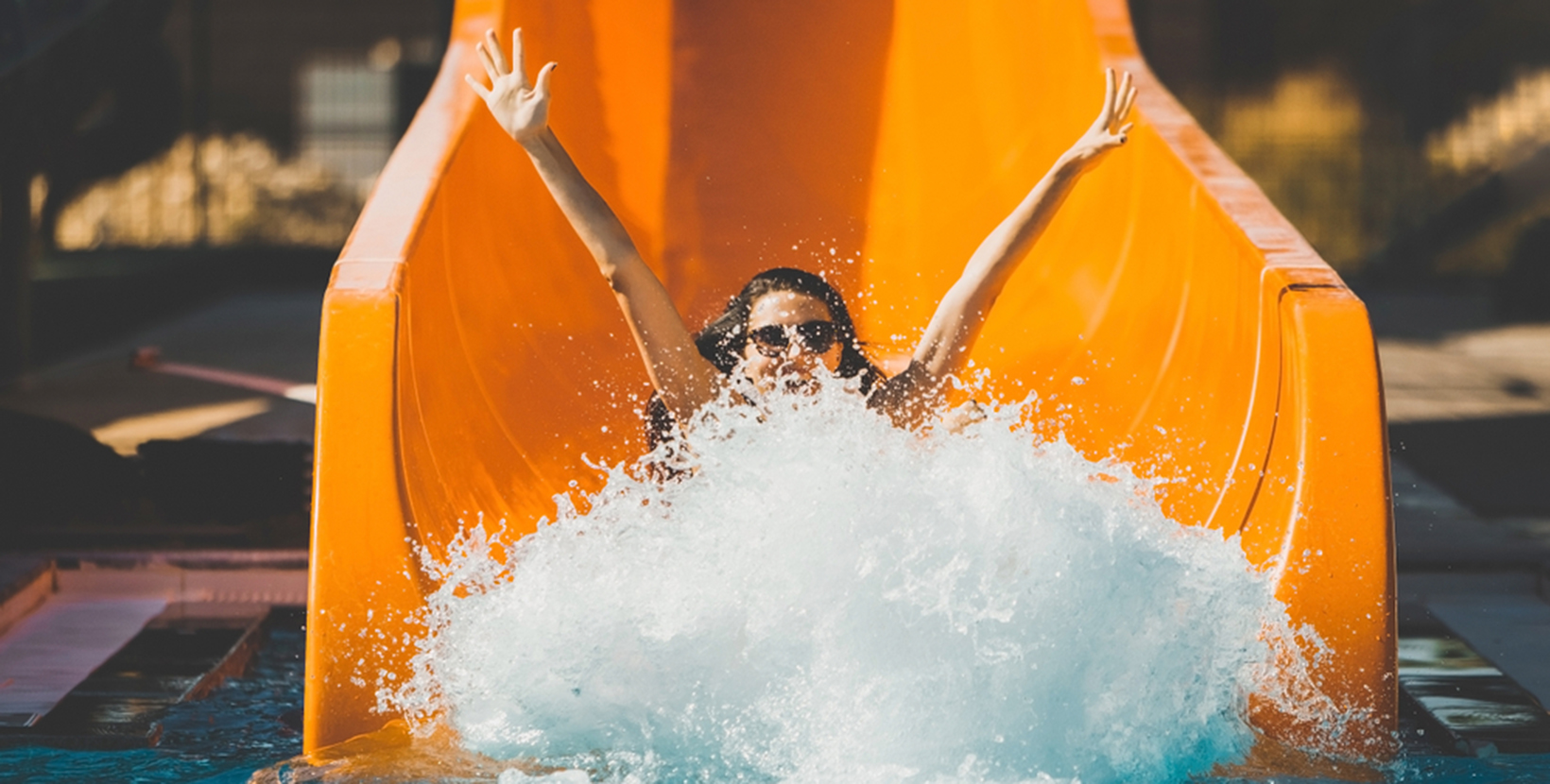 joyful woman going down on the rubber ring by the orange slide make the water splashing in the aqua park. Summer Vacation. Weekend on resort