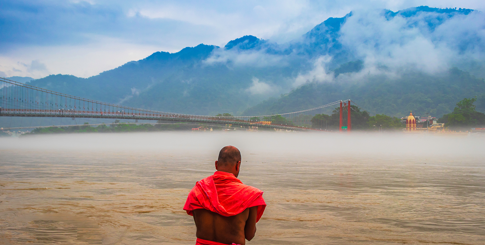 view of River Ganges, the famous bridge Ram Jhula surrounded by temples and mountains around in Rishikesh, India