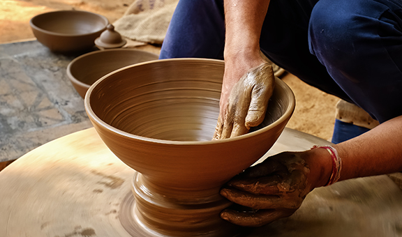 Pottery - skilled wet hands of potter shaping the clay on potter wheel. Pot, vase throwing. Manufacturing traditional handicraft Indian bowl, jar, pot, jug. Shilpagram, Udaipur, Rajasthan, India